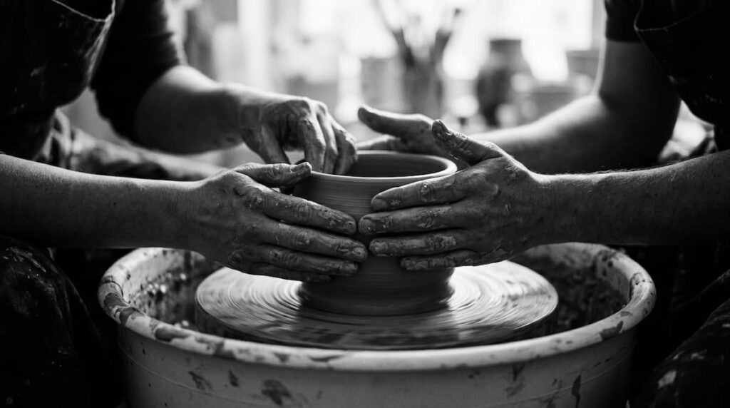 Two people shaping a clay pot together
